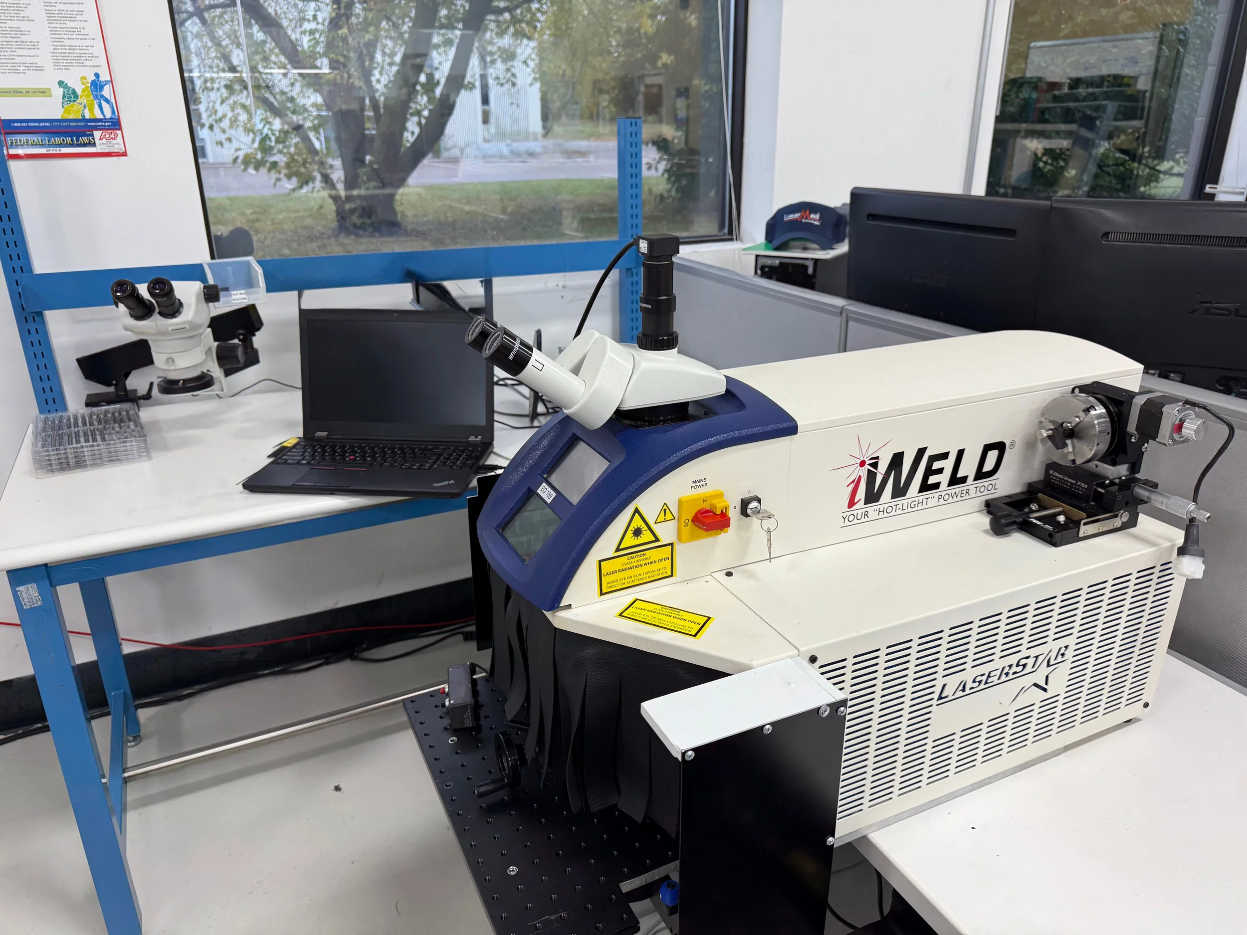 A Nd:YAG laser welding system with control panel and microscope in a laboratory research facility.