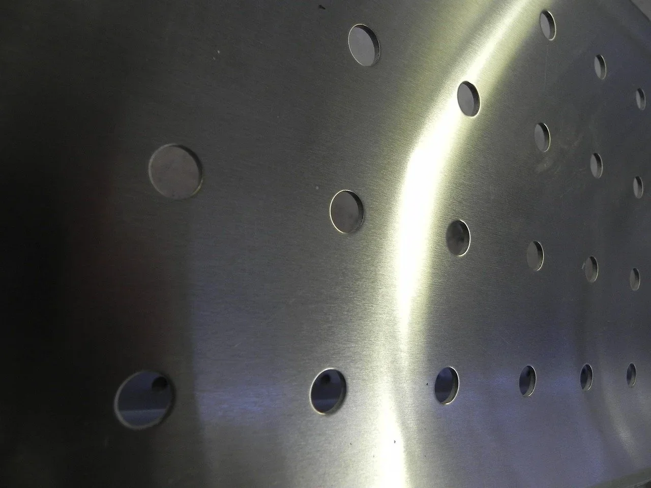 Perforated metal sheet with circular holes and bright light streaming through a vertical gap, showing industrial or architectural material detail.