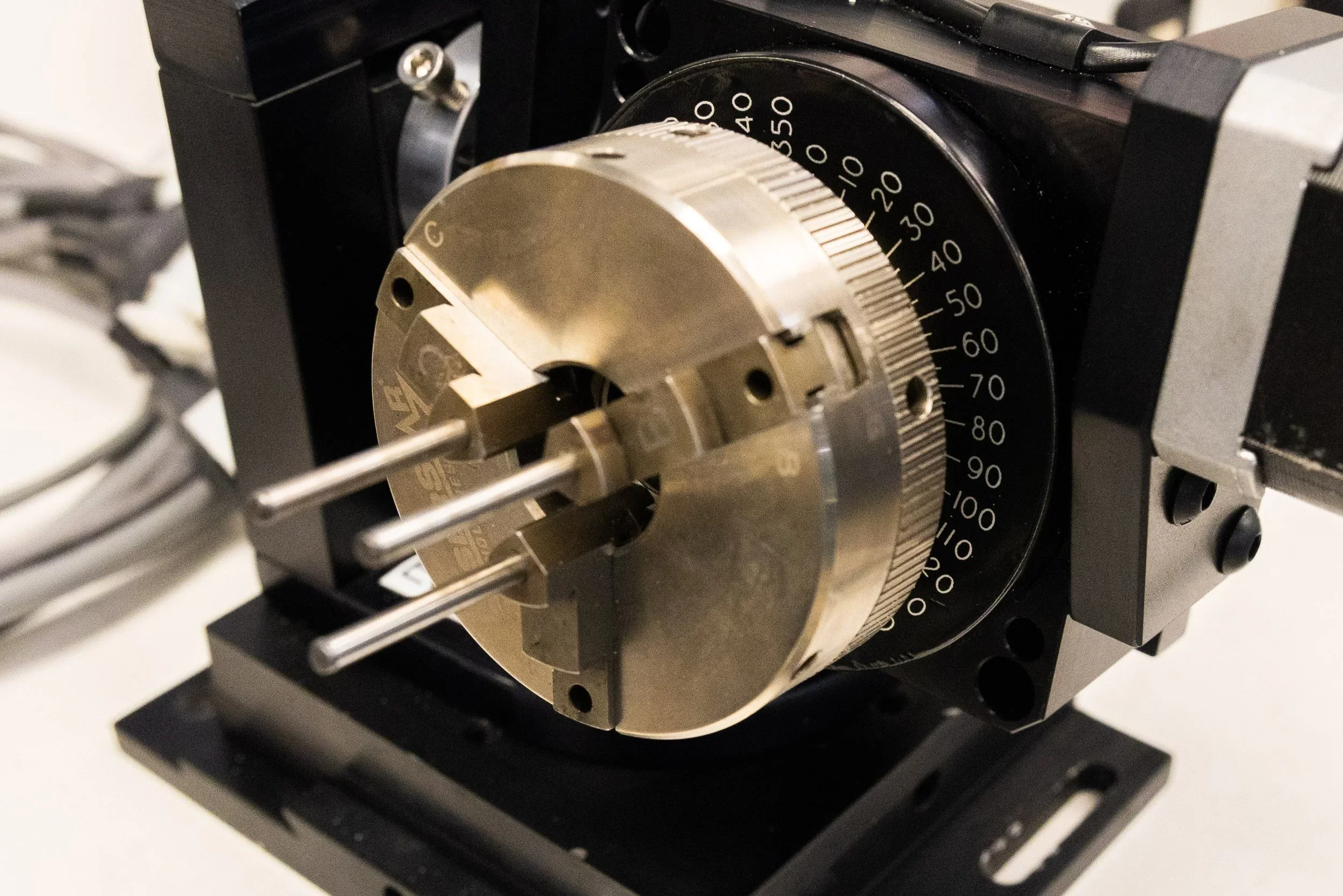 A precision measurement dial gauge mounted on a black metal frame in a laboratory or technical testing setting.
