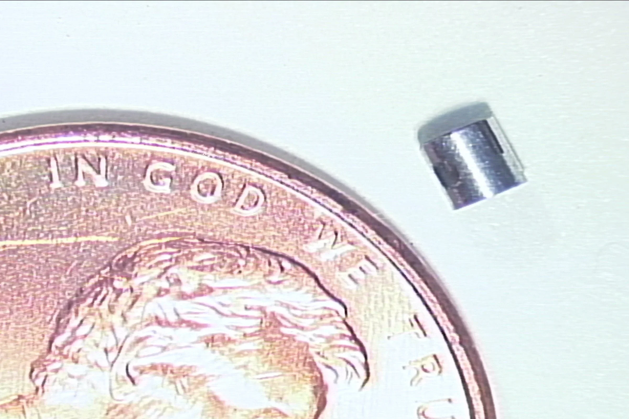 A small cylindrical magnet positioned next to a British pound coin for size comparison.