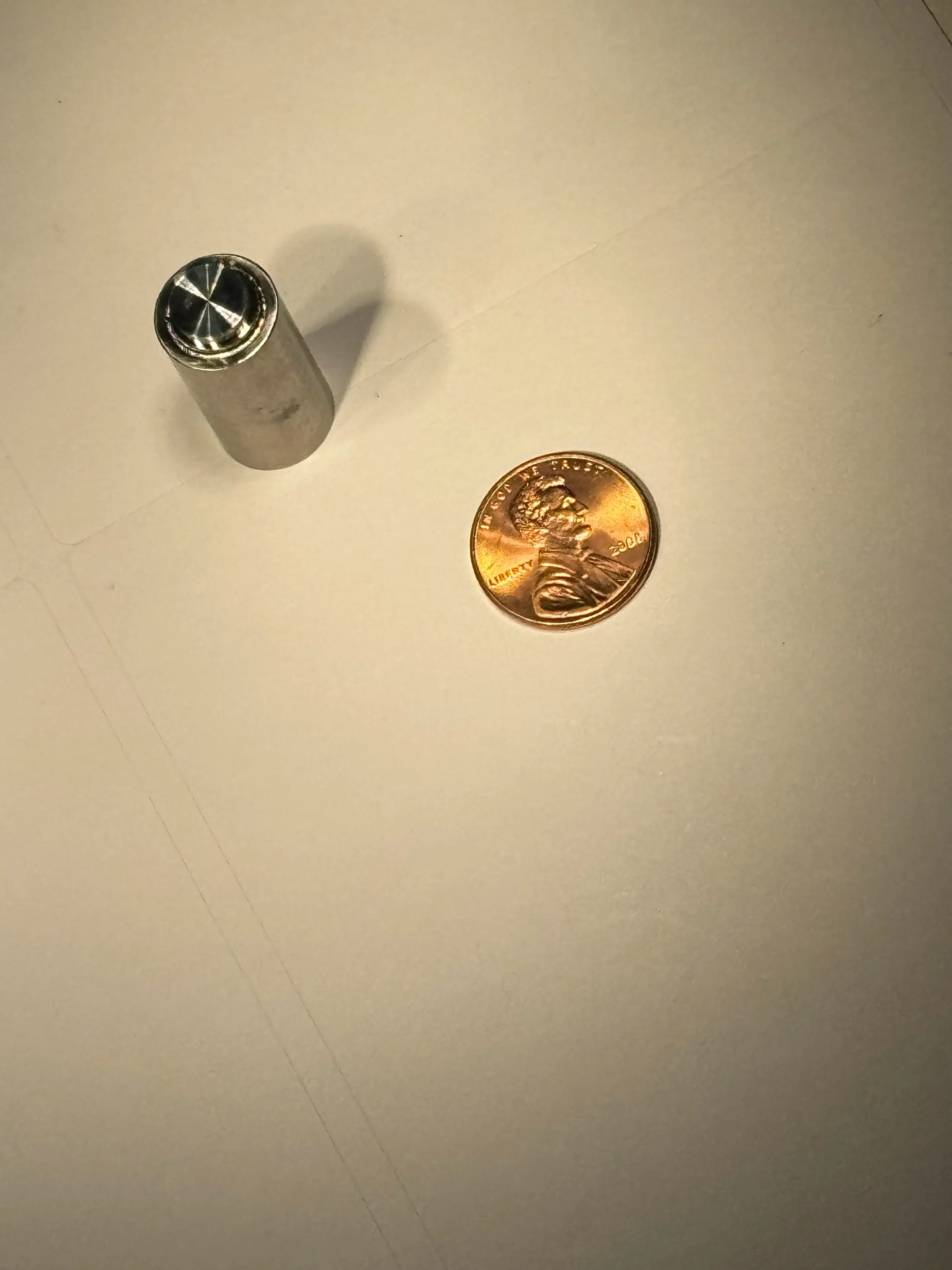 A small metal cylindrical object with a circular dial top displayed next to a penny for scale on a white surface.