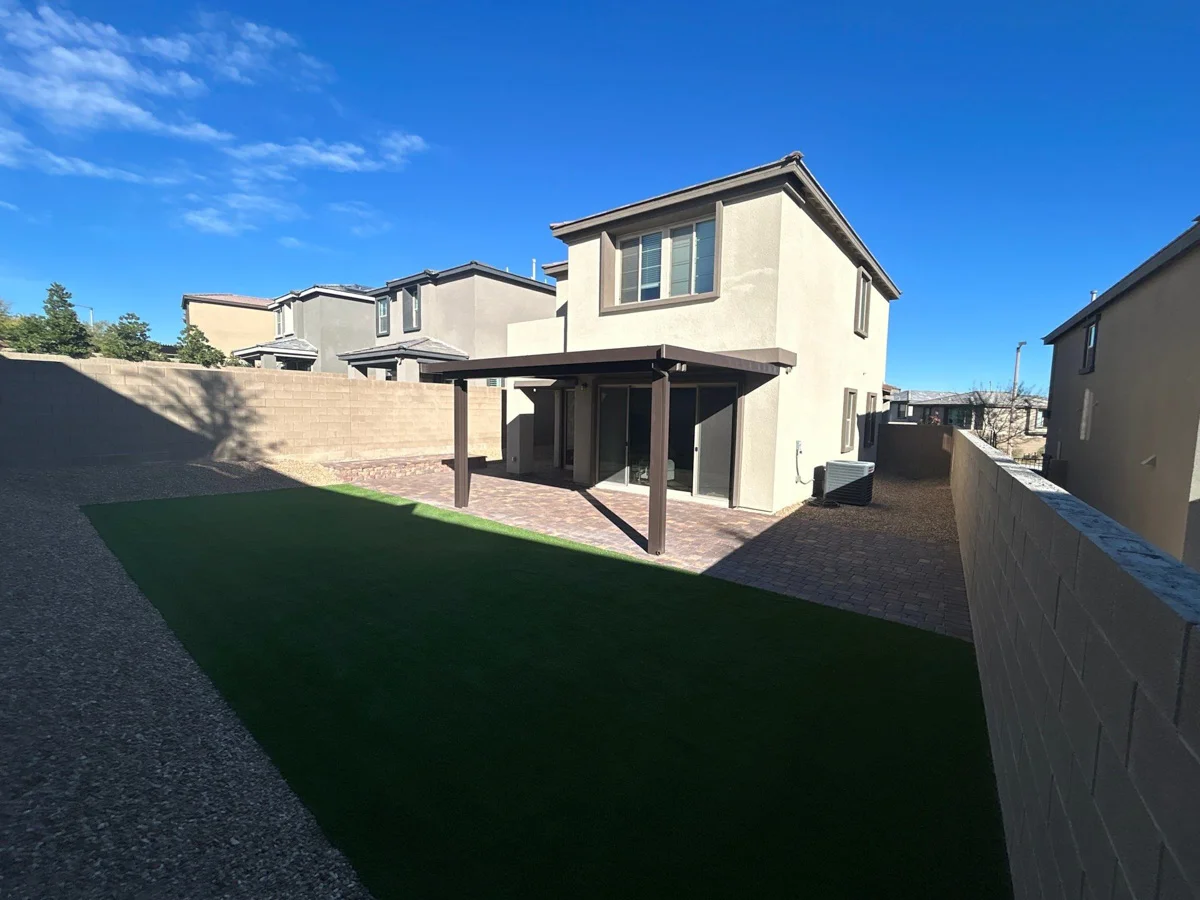 Artificial turf lawn installation in a residential backyard with patio and pergola.