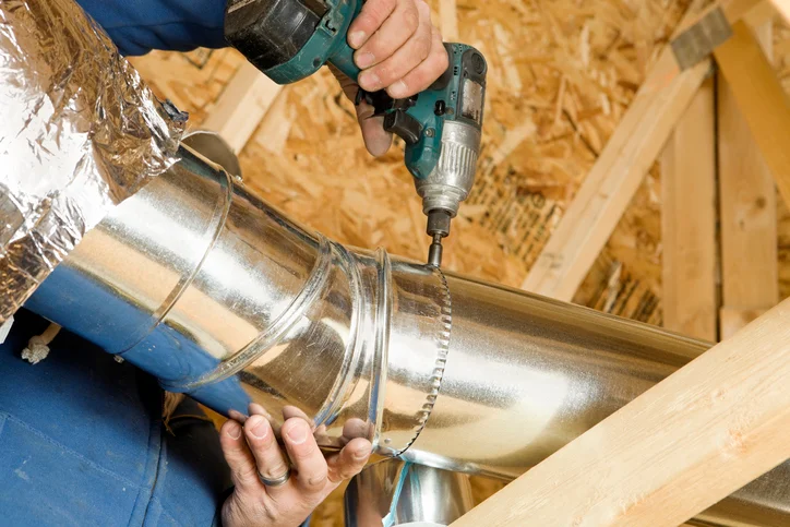Technician fastening a run of sheet-metal ductwork with a drill