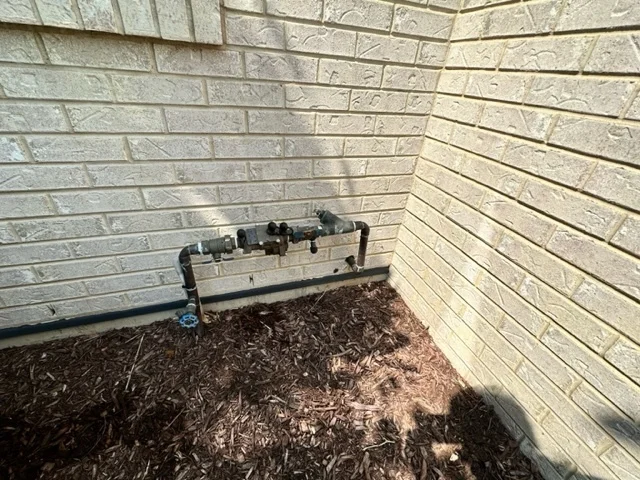 Irrigation drip line system installed along the foundation of a residential structure with mulch ground cover.