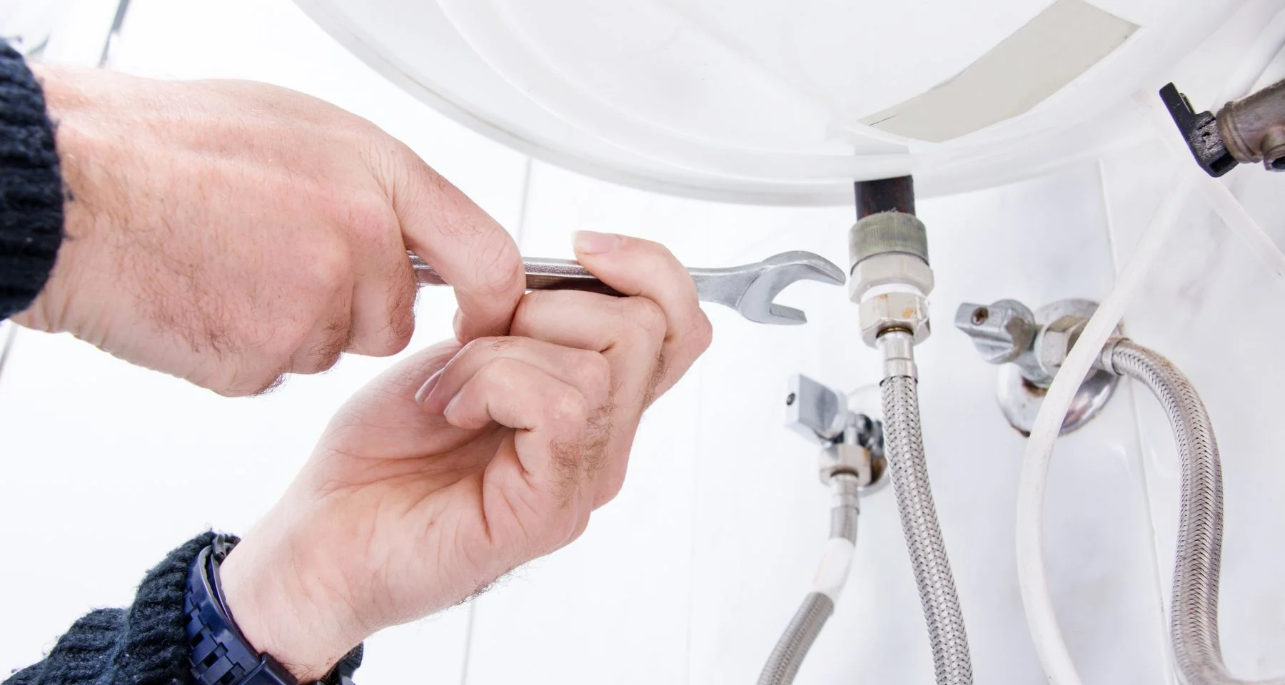 Hands tightening a water supply-line fitting with a wrench