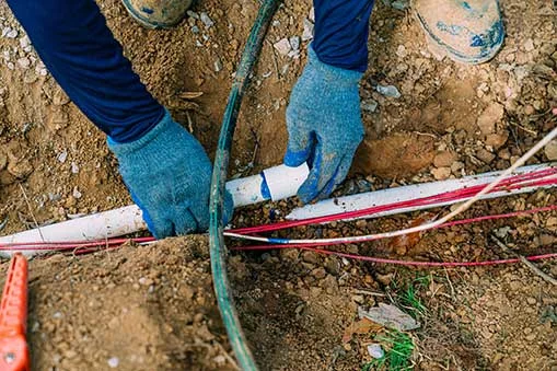 Underground irrigation and utility line installation work being performed in soil with green hose and white PVC pipe.