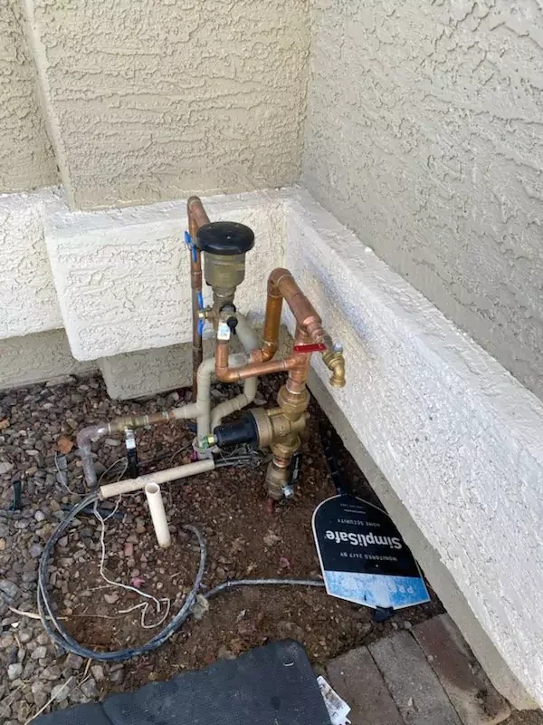 Outdoor water supply and drainage piping installation in a foundation/basement area showing copper and PVC pipes with brass valves and fittings.