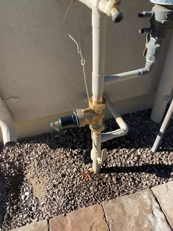 Outdoor water system pipe connections and valves installed in a gravel bed next to a residential foundation.