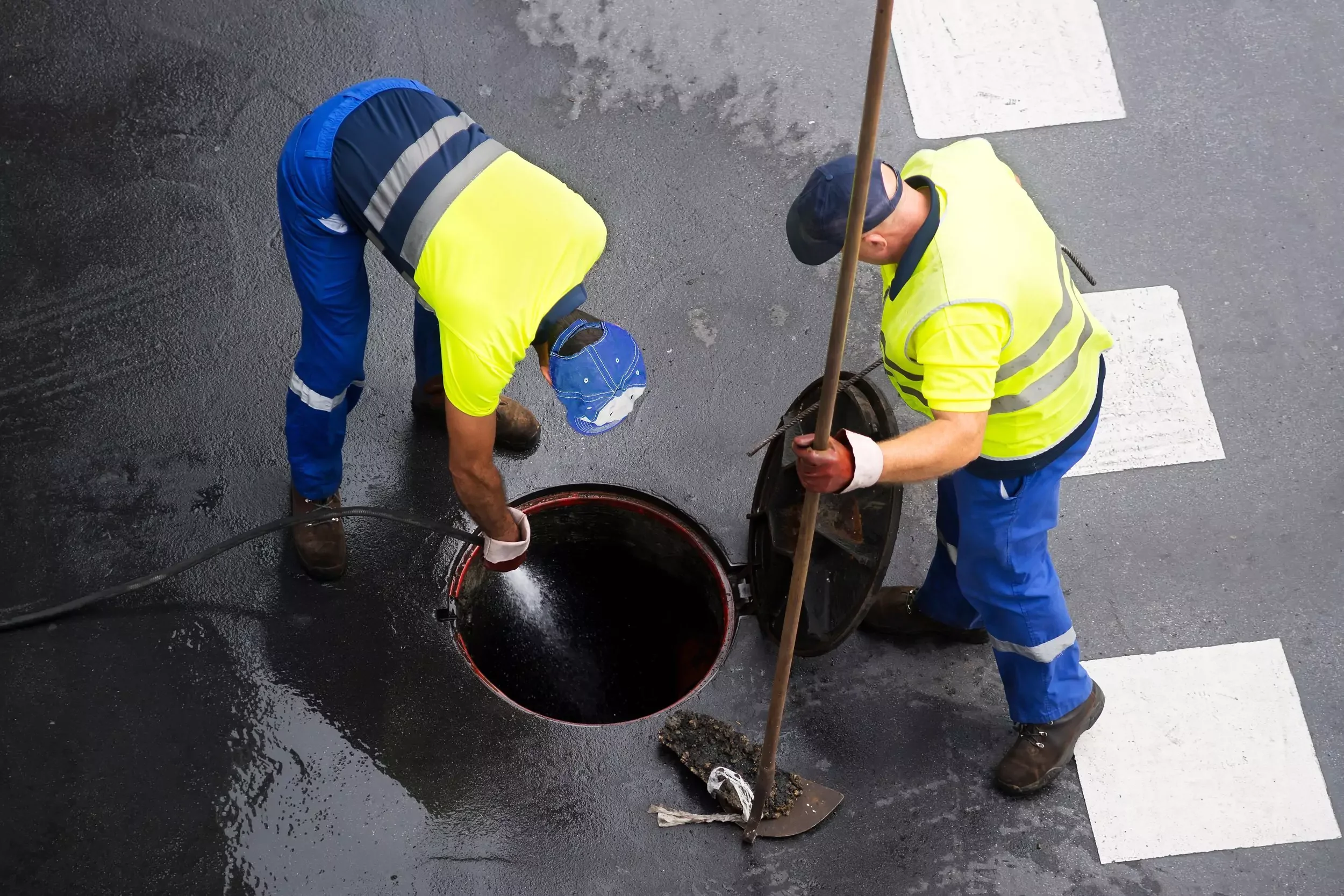 Sewer and drain cleaning work being performed on an open manhole access point in a wet street.