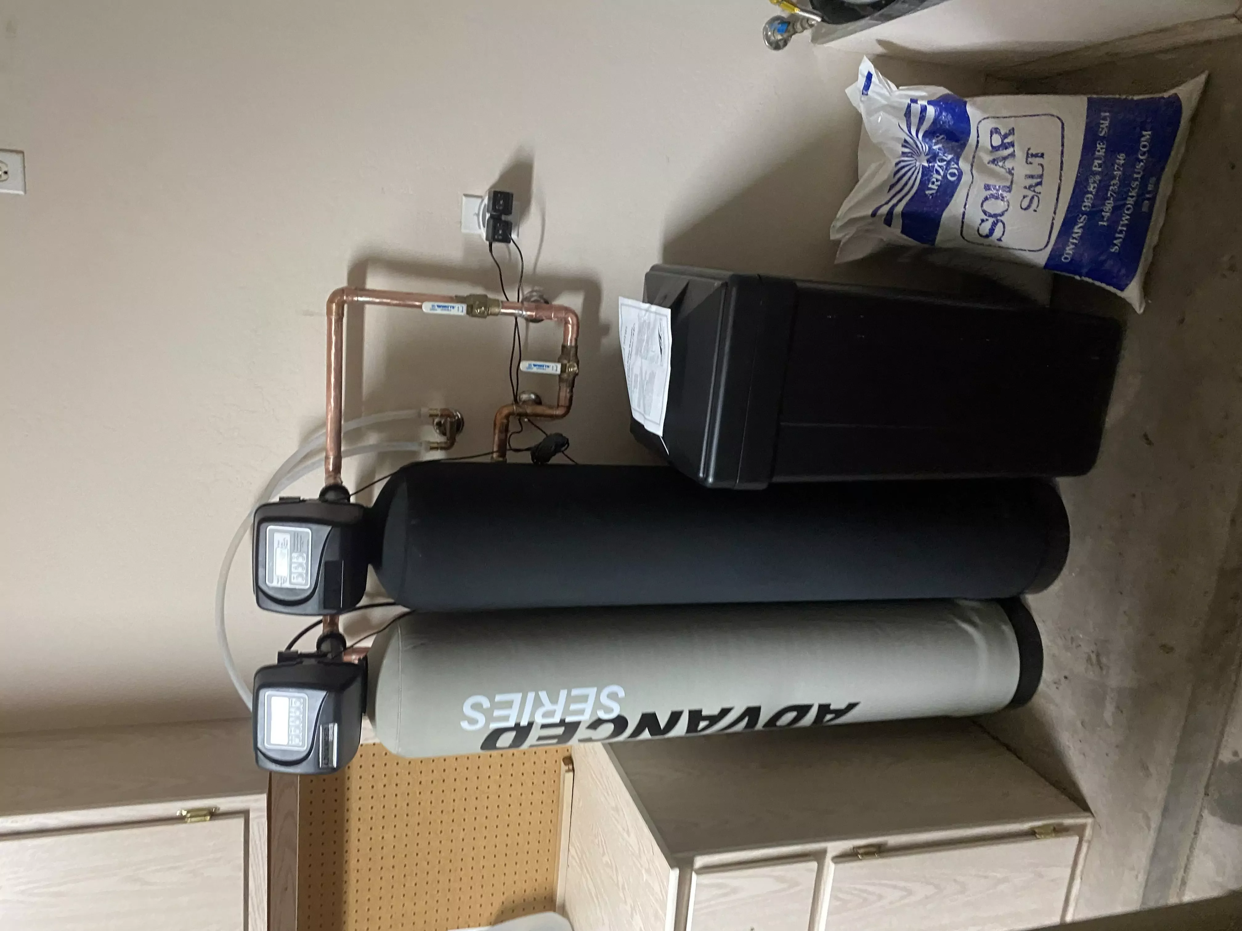Water filtration and softening system with dual tanks and copper piping installed in a utility space.