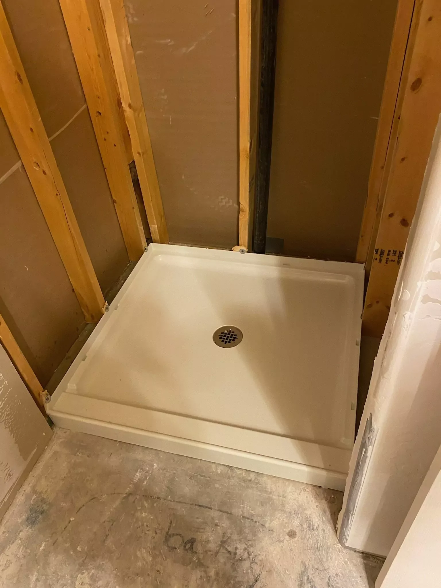 A white acrylic shower pan with center drain installed in a framed bathroom enclosure during construction.