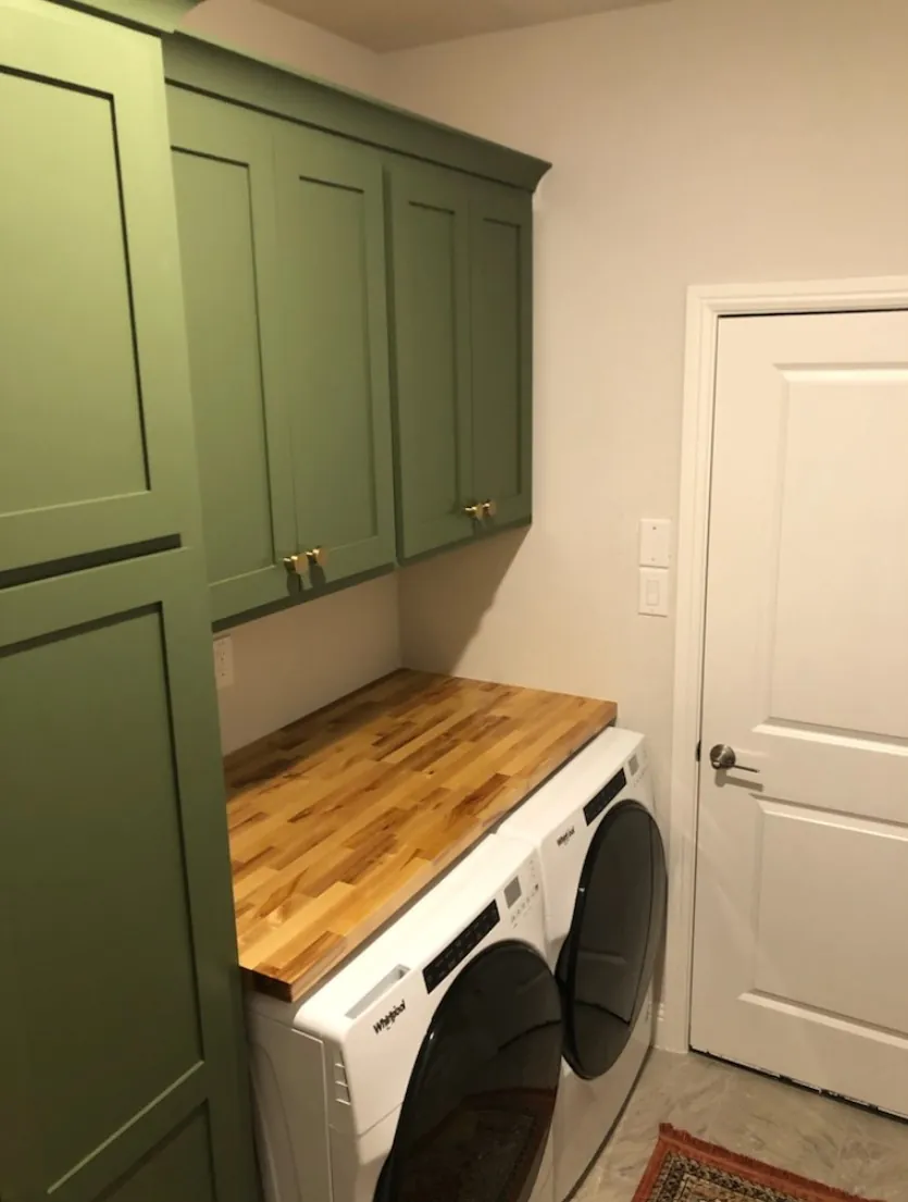 Green laundry cabinets with a butcher block counter over the machines