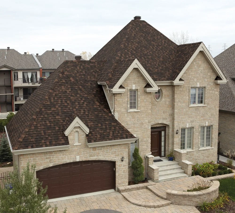 Architectural asphalt shingle roof installation on a two-story residential home with complex roofline featuring multiple peaks and valleys.