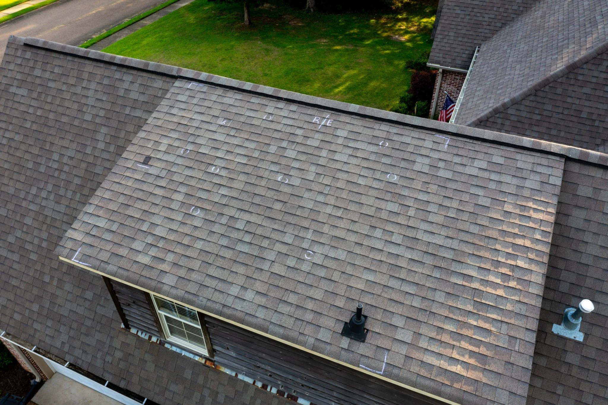Asphalt shingle roof installation or replacement on a residential home, photographed from above showing the roof plane with marked nail locations and the surrounding yard.
