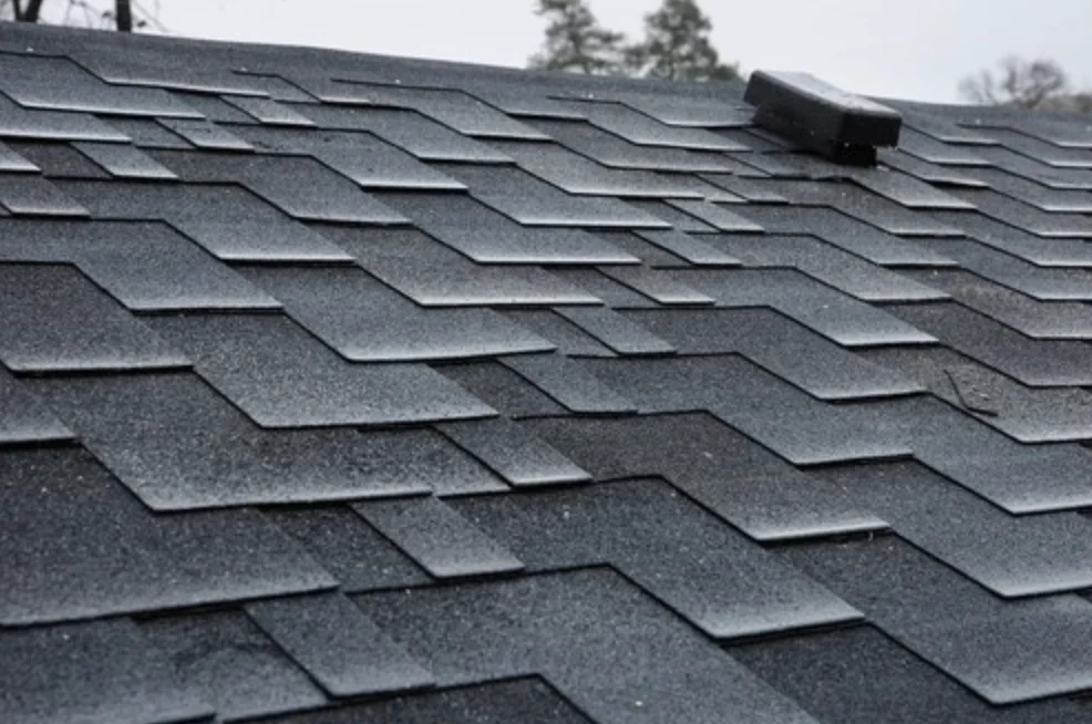 Asphalt shingles on a residential roof with a close-up view showing the layered installation and a roof vent.