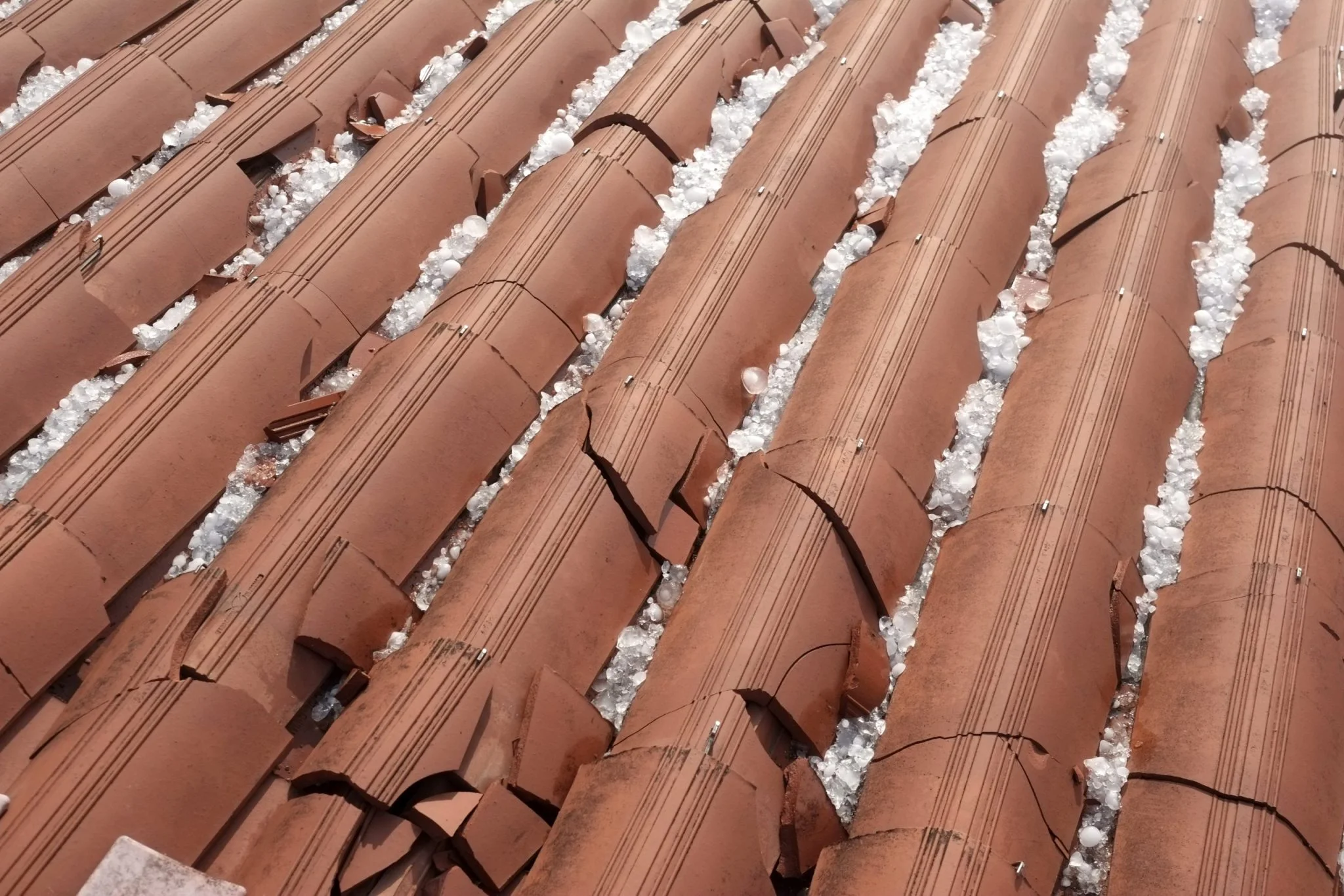 Clay barrel tile roofing with accumulated snow and ice deposits in a close-up overhead view.