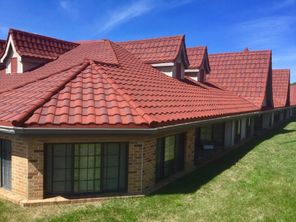 Clay tile roof installation on a brick residential home with multiple gables and dormers in a suburban setting.