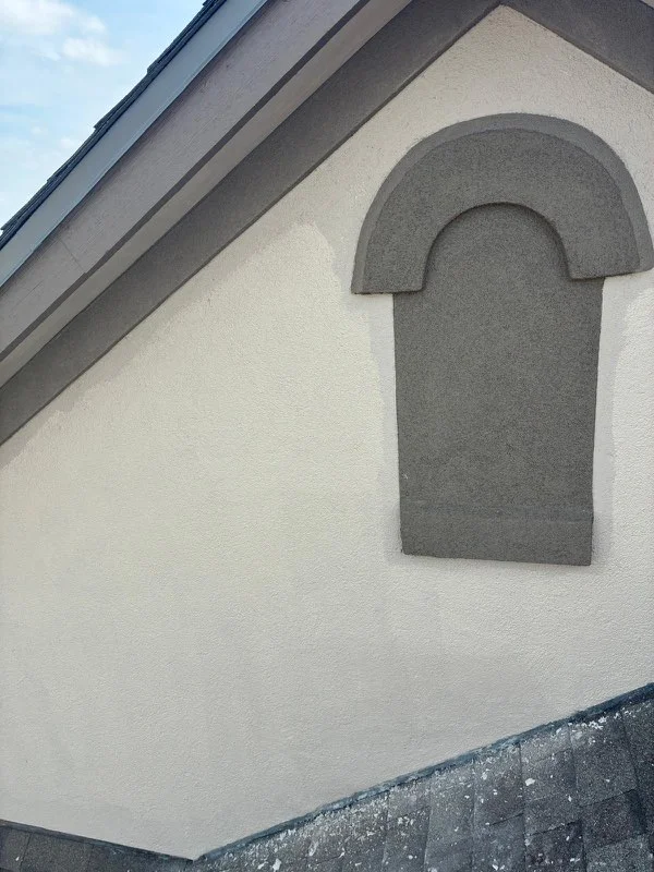 A gray chimney cap or roof flashing detail installed on a white exterior wall near the roofline.