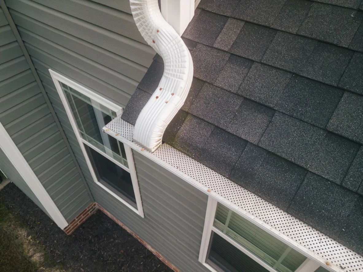 Gutter installation and roof edge detail work on a residential home showing white K-style gutters and downspout along the roofline.