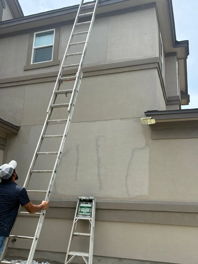Ladder access and exterior wall work during what appears to be a roof or siding project on a residential home.