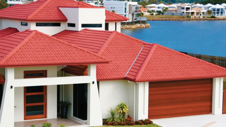 Metal roof installation on a modern residential home with red corrugated metal roofing in a waterfront setting.
