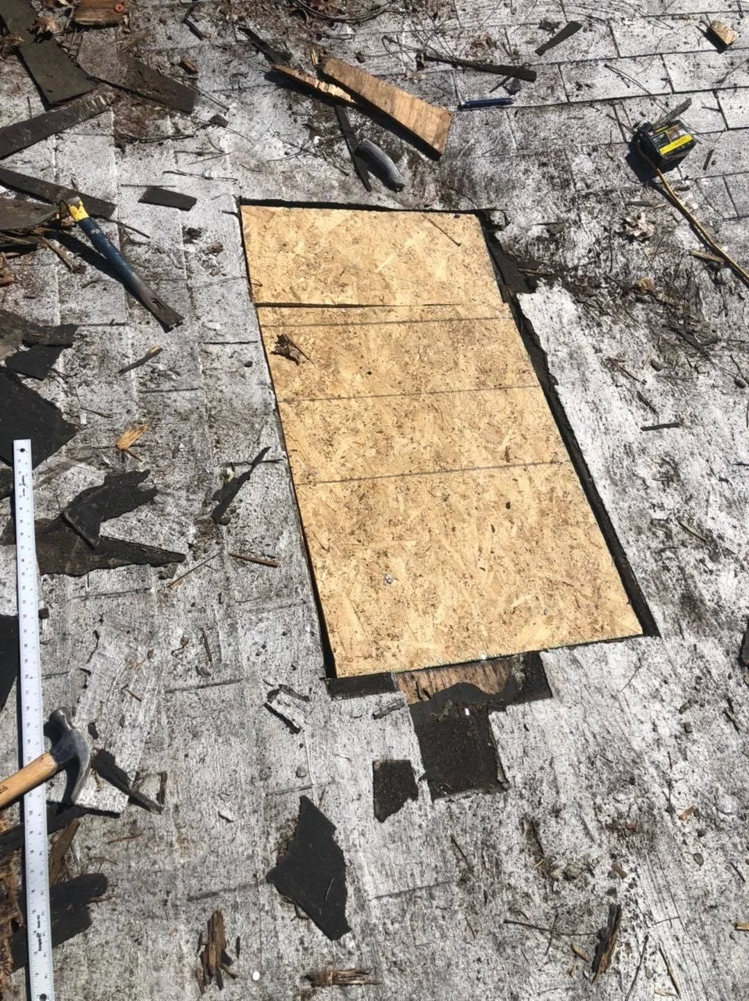 Roof decking installation in progress on a flat roof with plywood sheets laid out and construction tools scattered across the work surface.