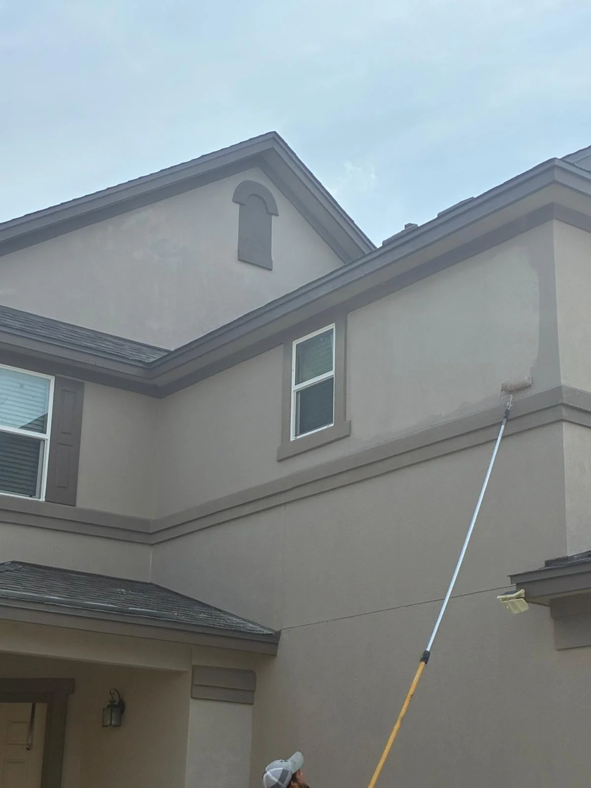 Roof inspection or assessment of a residential home's exterior, showing the gable end and upper wall sections with a measurement pole positioned against the structure.