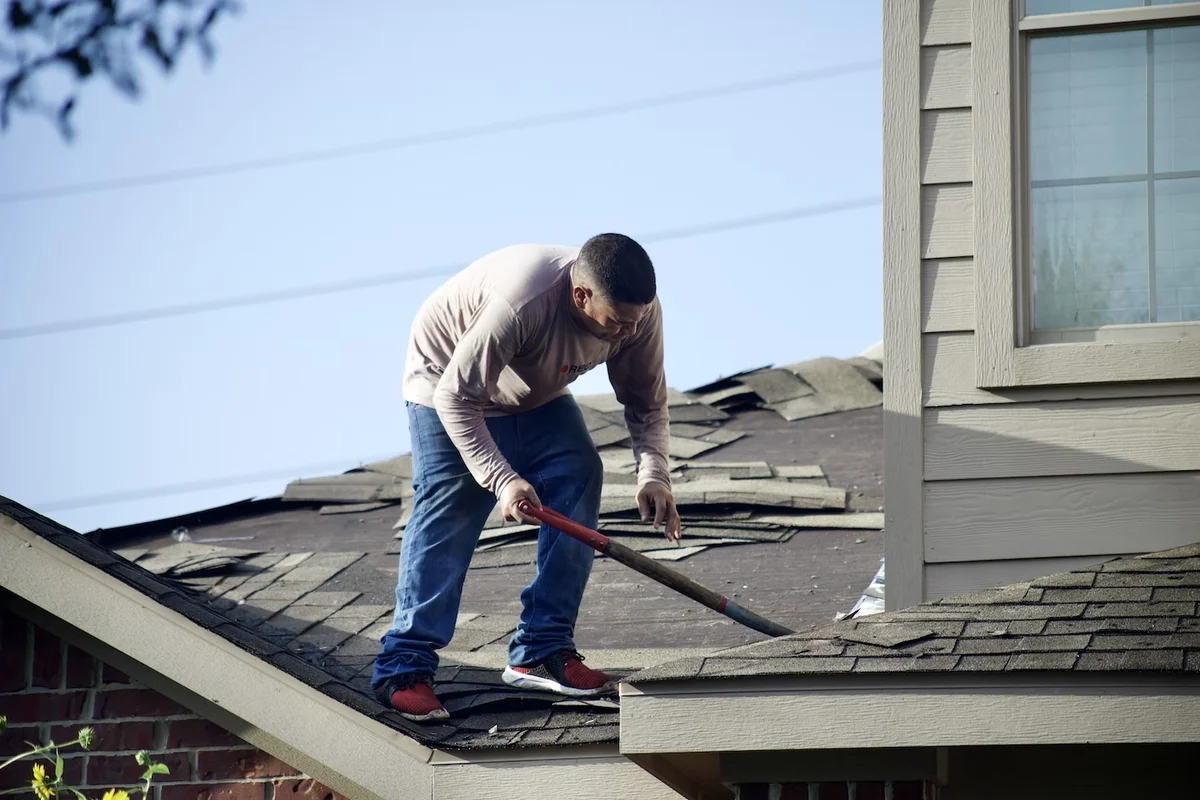 Roof repair work being performed on a residential asphalt shingle roof with visible damage and deterioration.