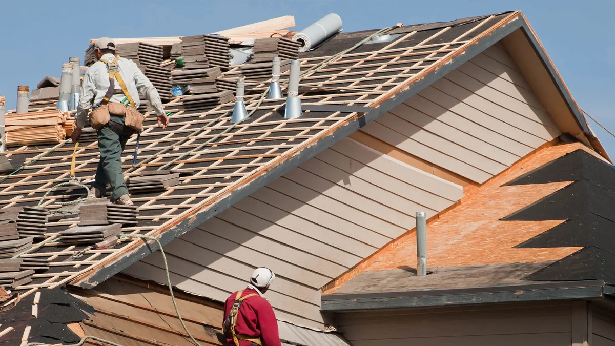 Roof replacement work in progress, showing workers removing old shingles and exposing the roof structure and sheathing on a residential home.