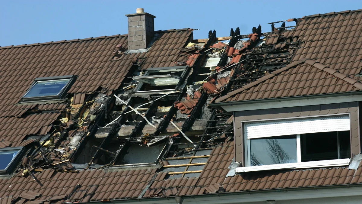 Roof replacement work in progress showing damaged roof structure with removed tiles and exposed framing on a residential home.