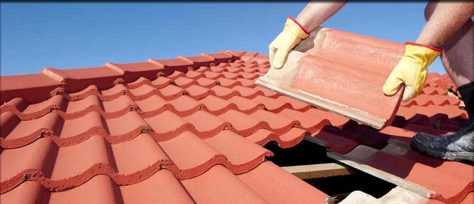 Roof tile replacement work being performed on a red clay tile roof in bright daylight.