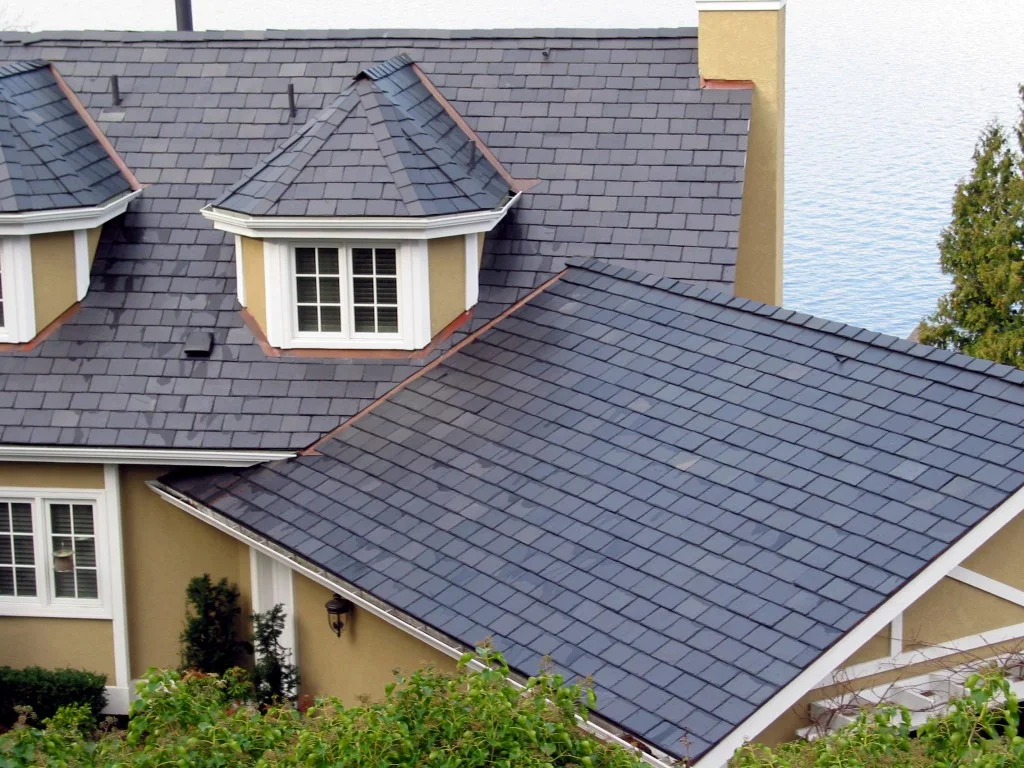 Slate and asphalt shingle roof installation on a two-story residential home with multiple roof planes, dormers, and a cupola near a waterfront setting.