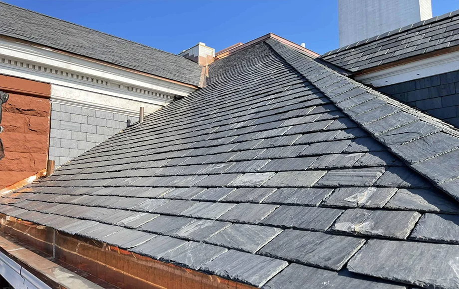 Slate tile roof installation on a residential home showing multiple roof planes and valleys with dark gray shingles.