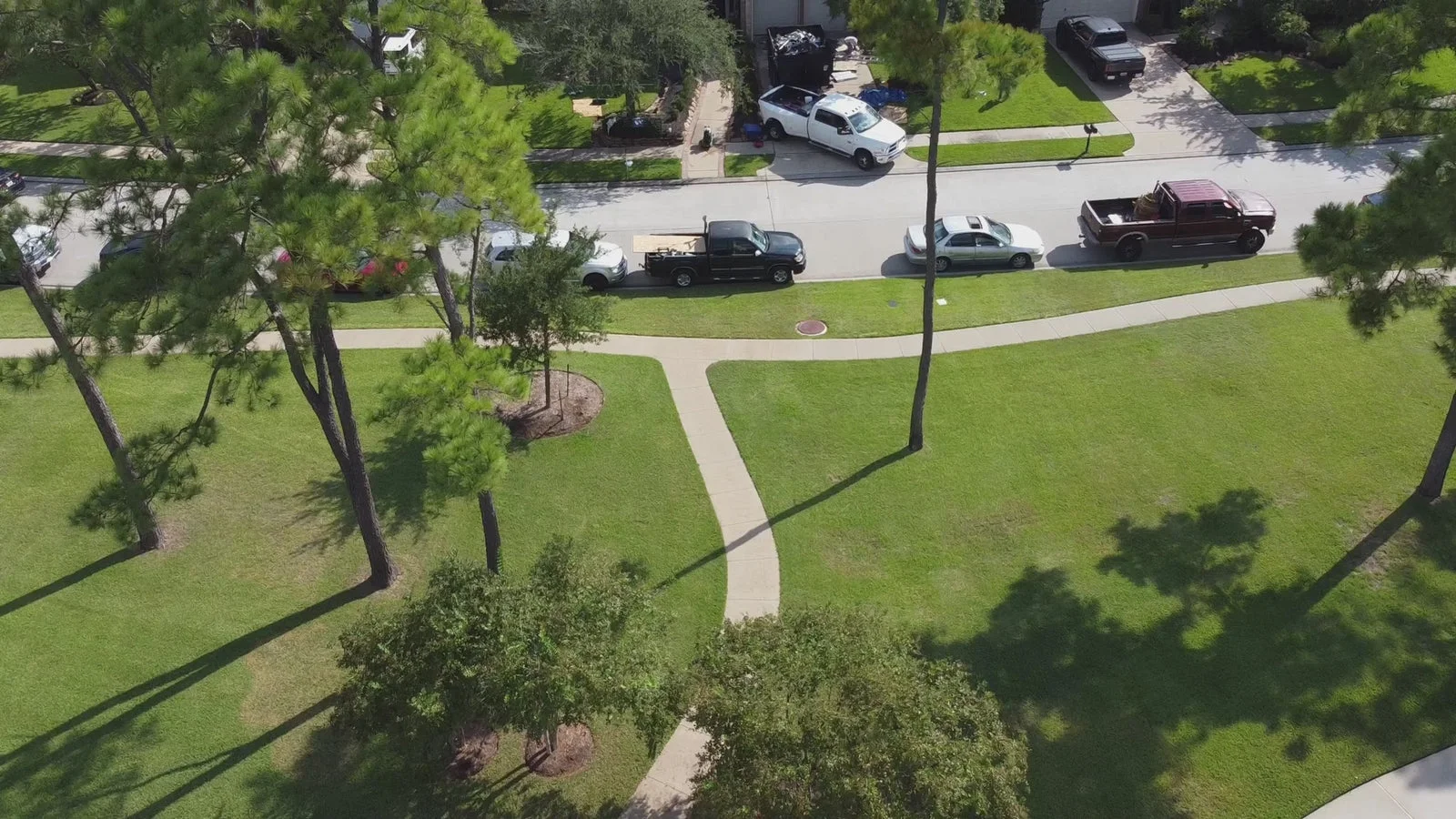 An aerial view of a residential neighborhood street with parked vehicles and landscaped yards, not showing any roofing work, materials, or services.