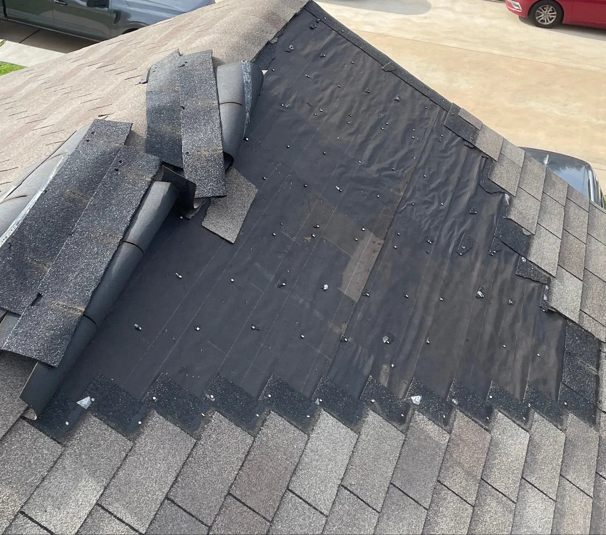 Asphalt shingle roof installation and repair work in progress on a residential home, showing roof underlayment, ventilation pipe, and partially installed shingles.