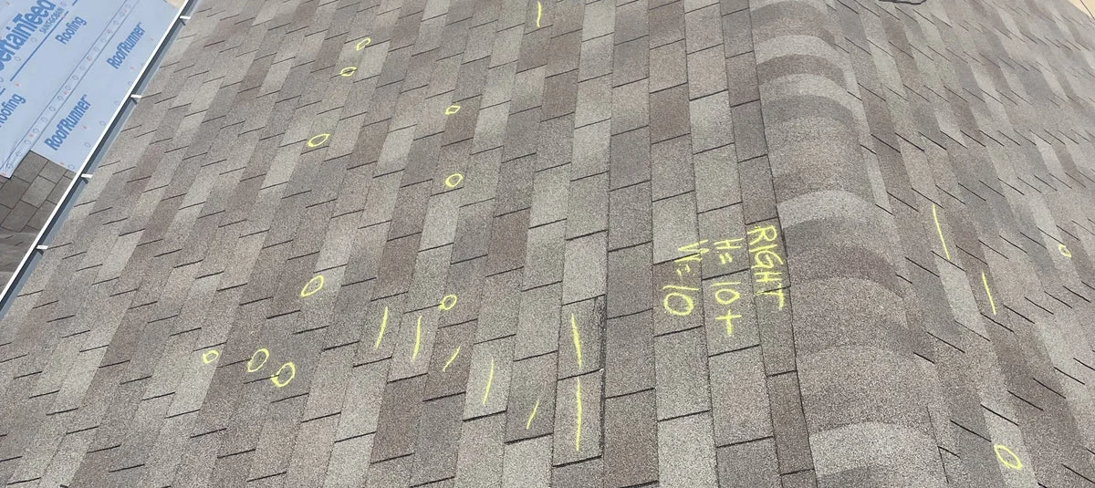 Asphalt shingle roof with yellow inspection markings and measurement annotations on the exterior surface.