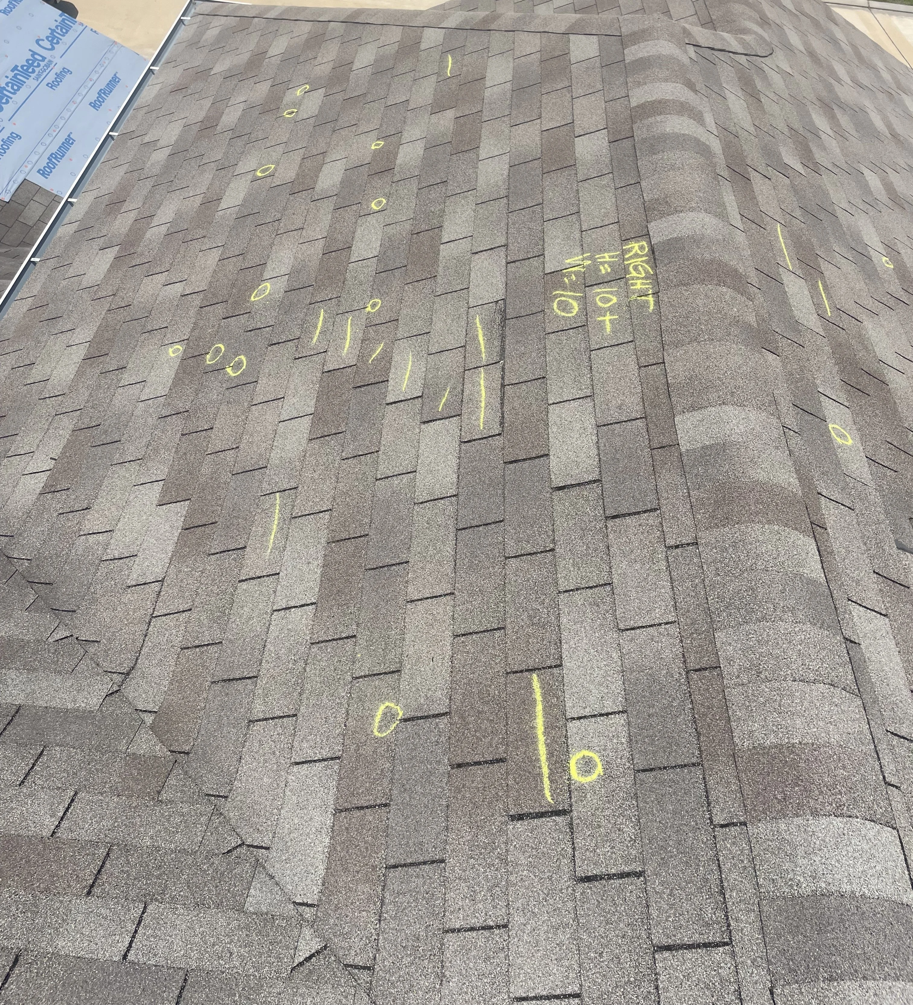 Asphalt shingle roof with yellow inspection markings and chalk notation visible on the exterior roof surface.