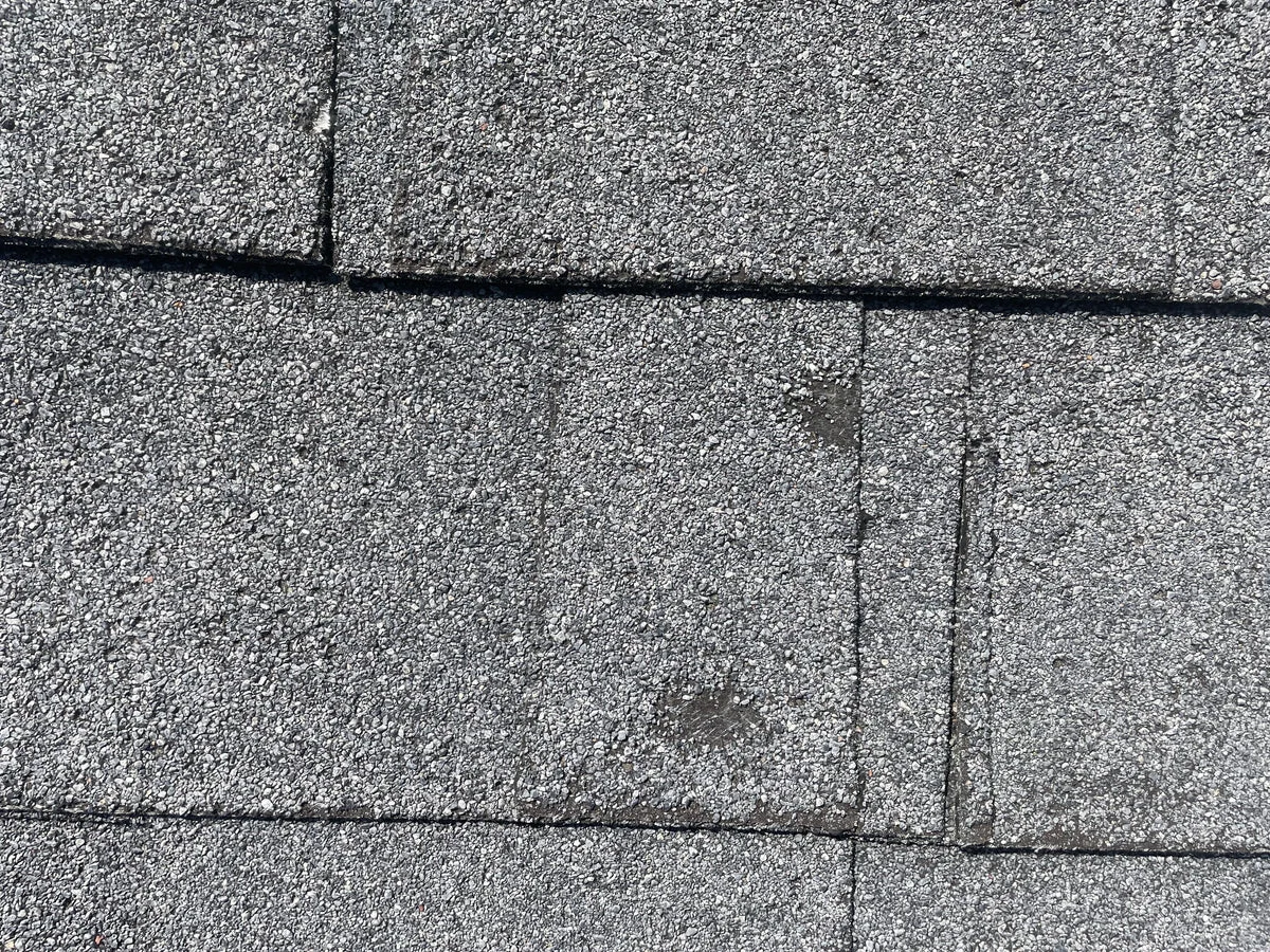 Asphalt shingle roofing material showing close-up detail of installed roof shingles with visible seams and granule texture on an exterior surface.