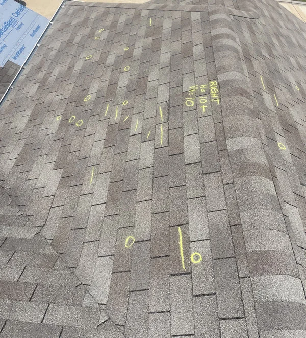 Asphalt shingle roofing with yellow inspection markings visible on the roof surface during an assessment or quality control process.