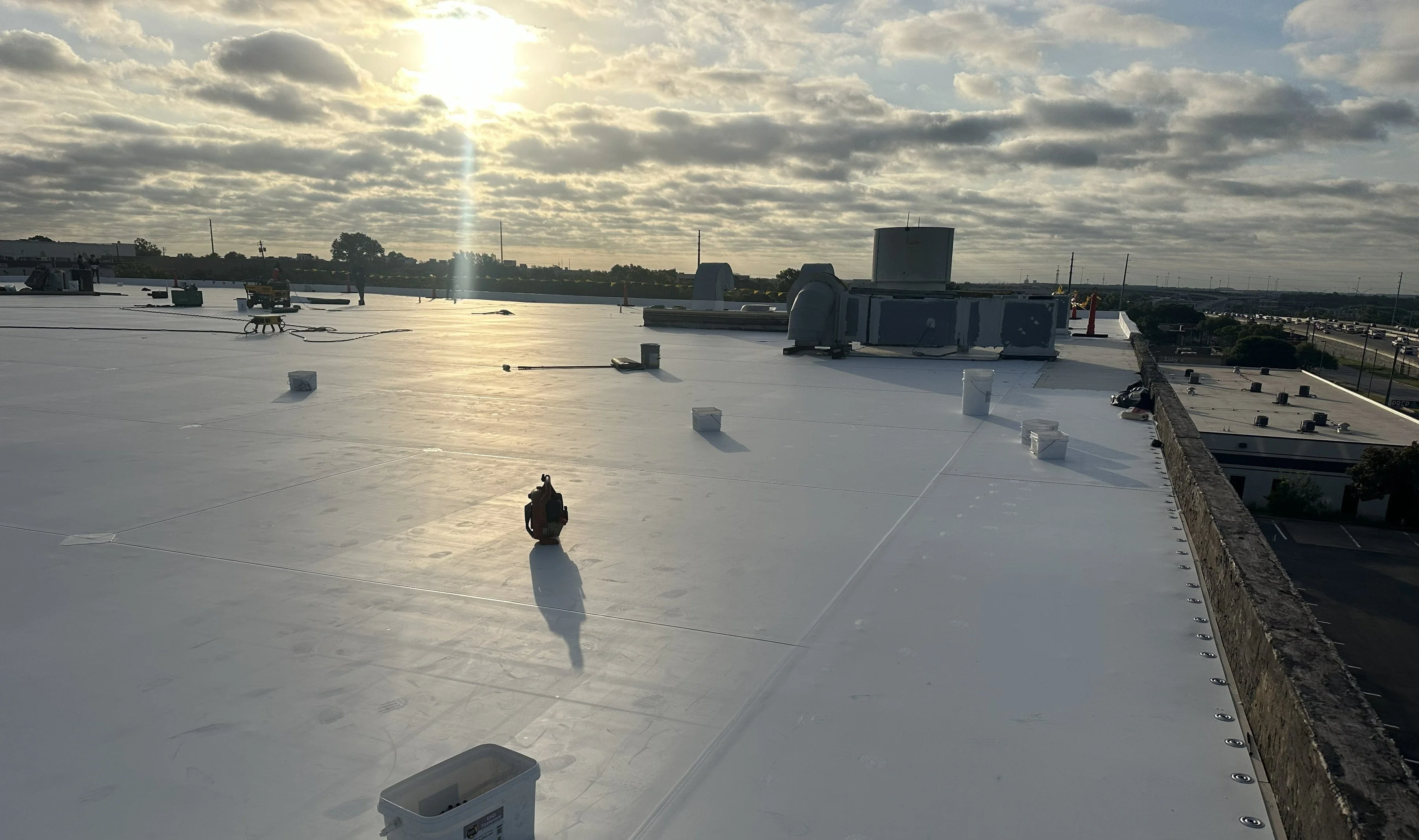 Flat roof membrane installation in progress on a commercial building overlooking a waterway and industrial area.