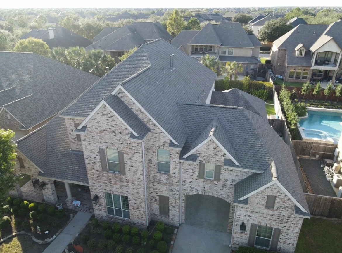A newly installed asphalt shingle roof on a two-story brick residential home in a suburban neighborhood.