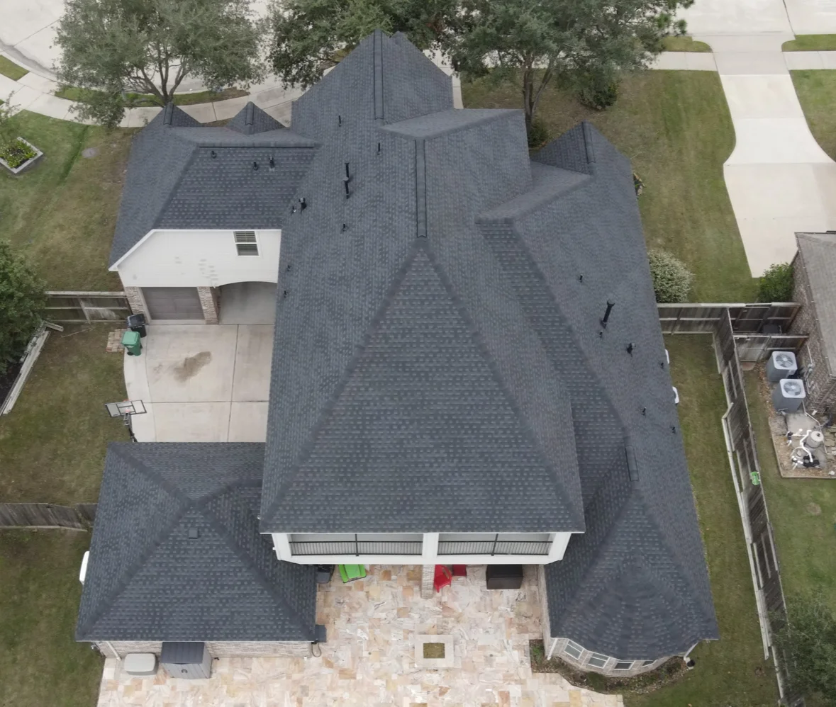 A newly installed dark gray asphalt shingle roof on a residential home with multiple peaks and valleys, shown in an aerial view of the completed project.