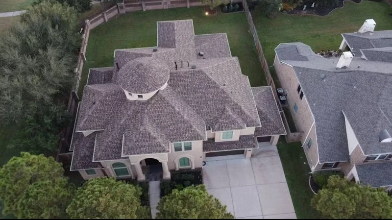 Residential roof installation and shingle work on a two-story home with complex roofline and multiple roof planes in an established neighborhood.