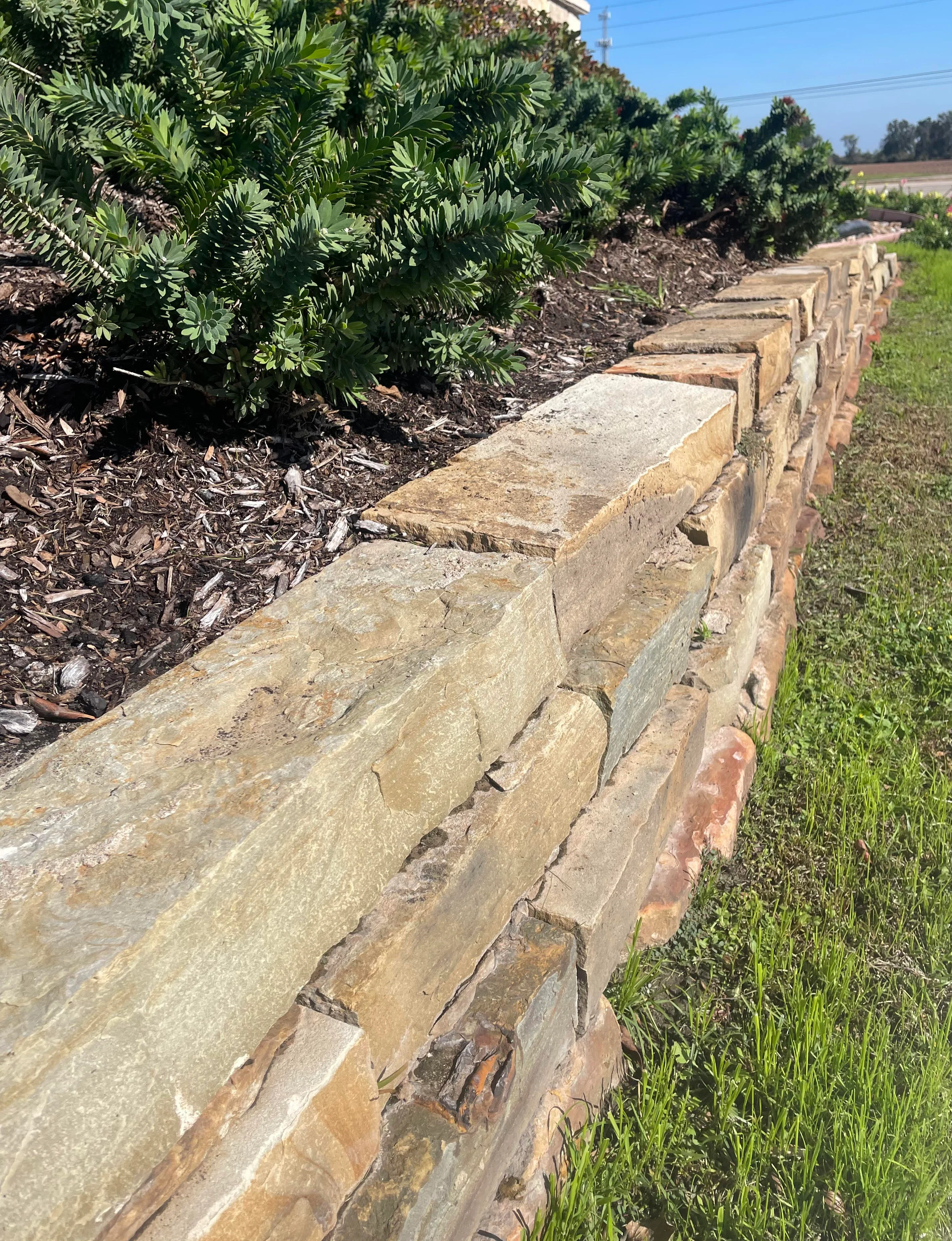 A stone retaining wall with landscape edging in an outdoor garden or property setting, unrelated to roofing contractor services.