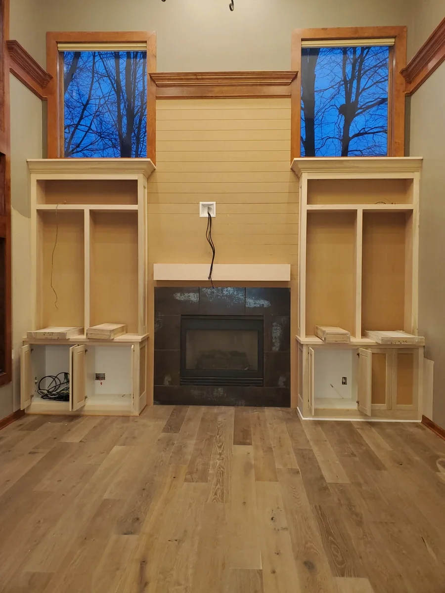 Custom built-in cabinetry and shelving flanking a fireplace in a residential living room with large windows.
