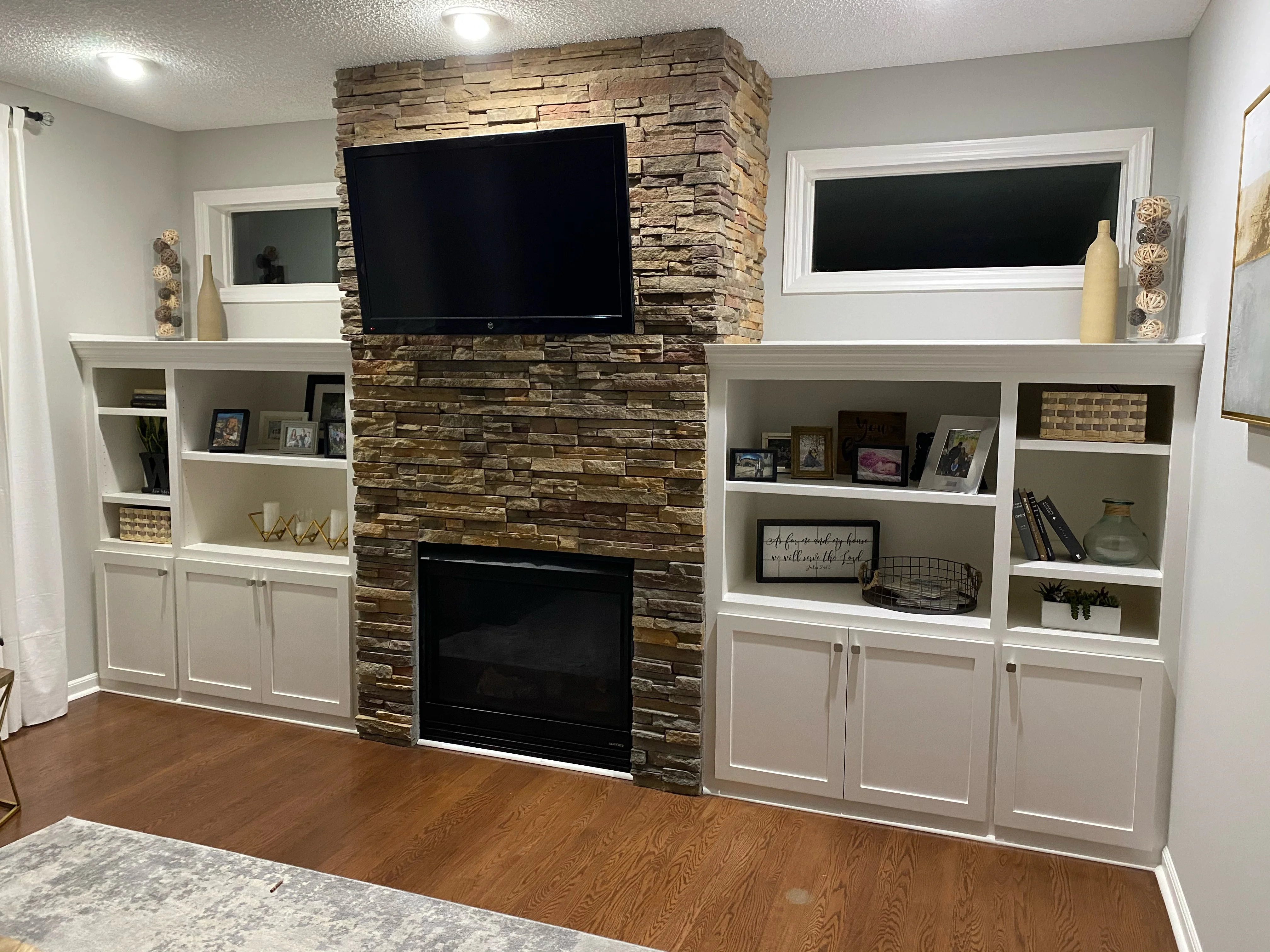 Built-in shelving and cabinetry beside a stone fireplace