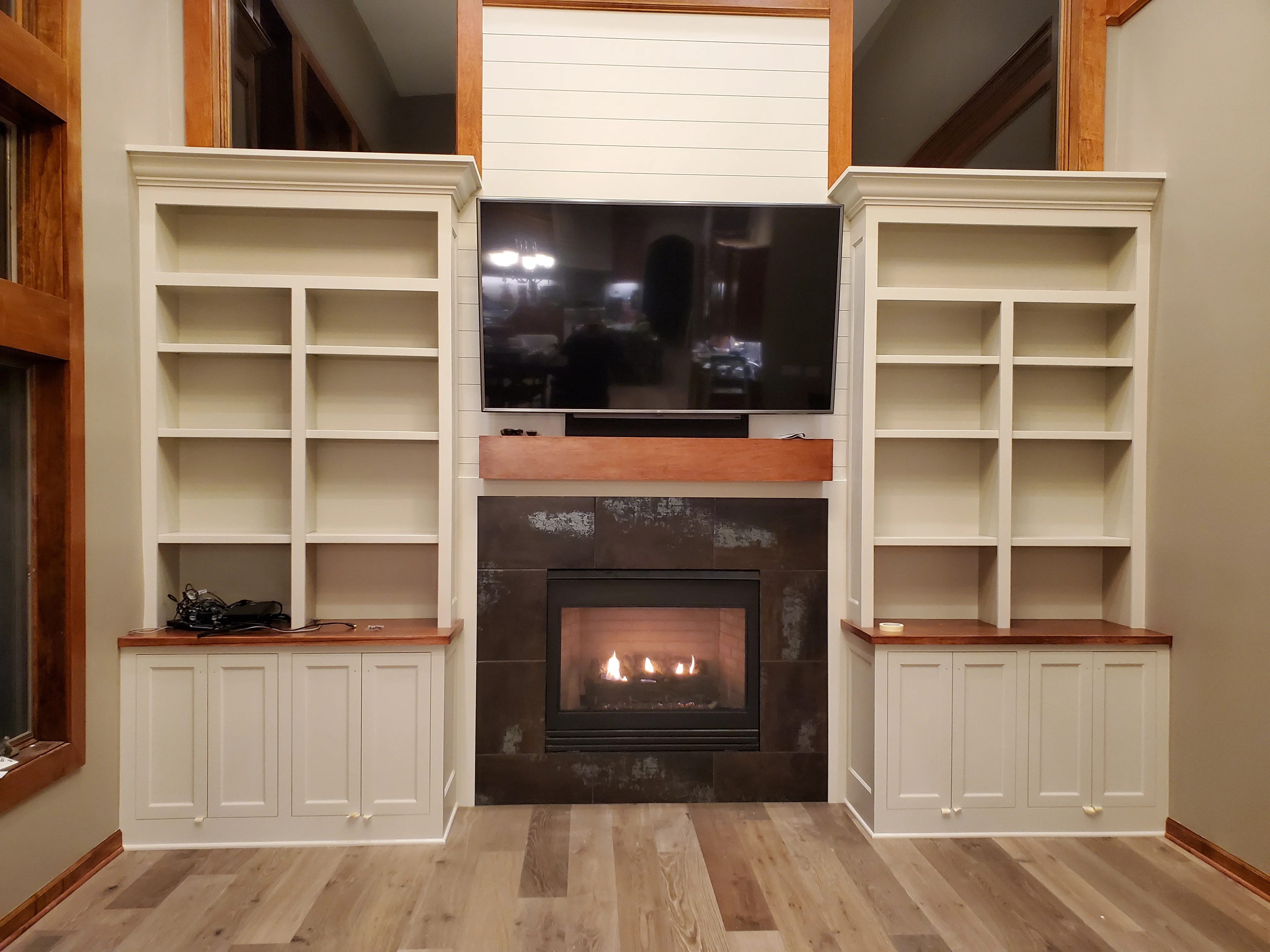 Custom built-in shelving with white cabinetry flanking a fireplace and mounted television in a modern living room.