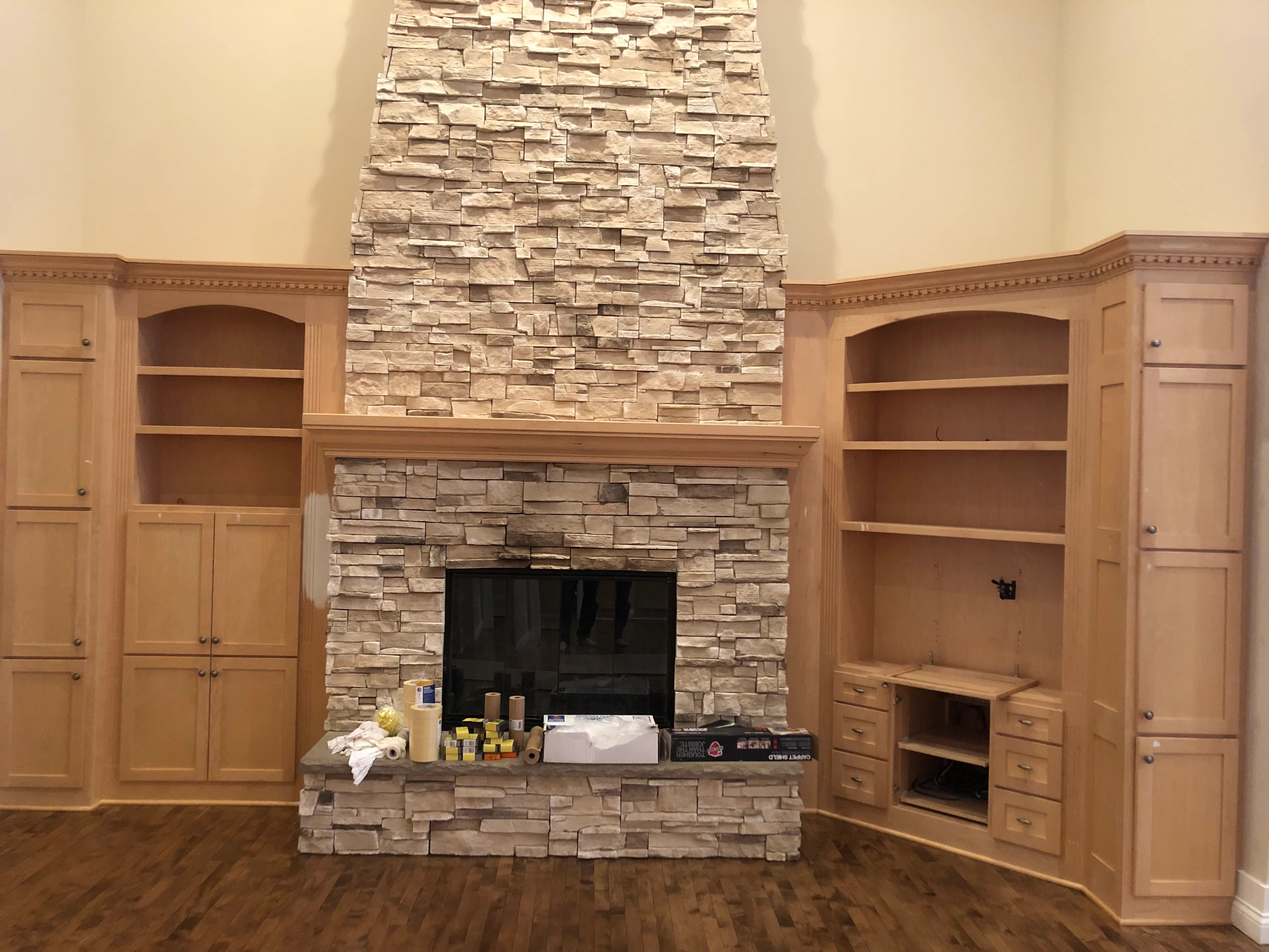 Custom built-in wooden cabinetry with shelving flanking a stone fireplace in a residential living room.