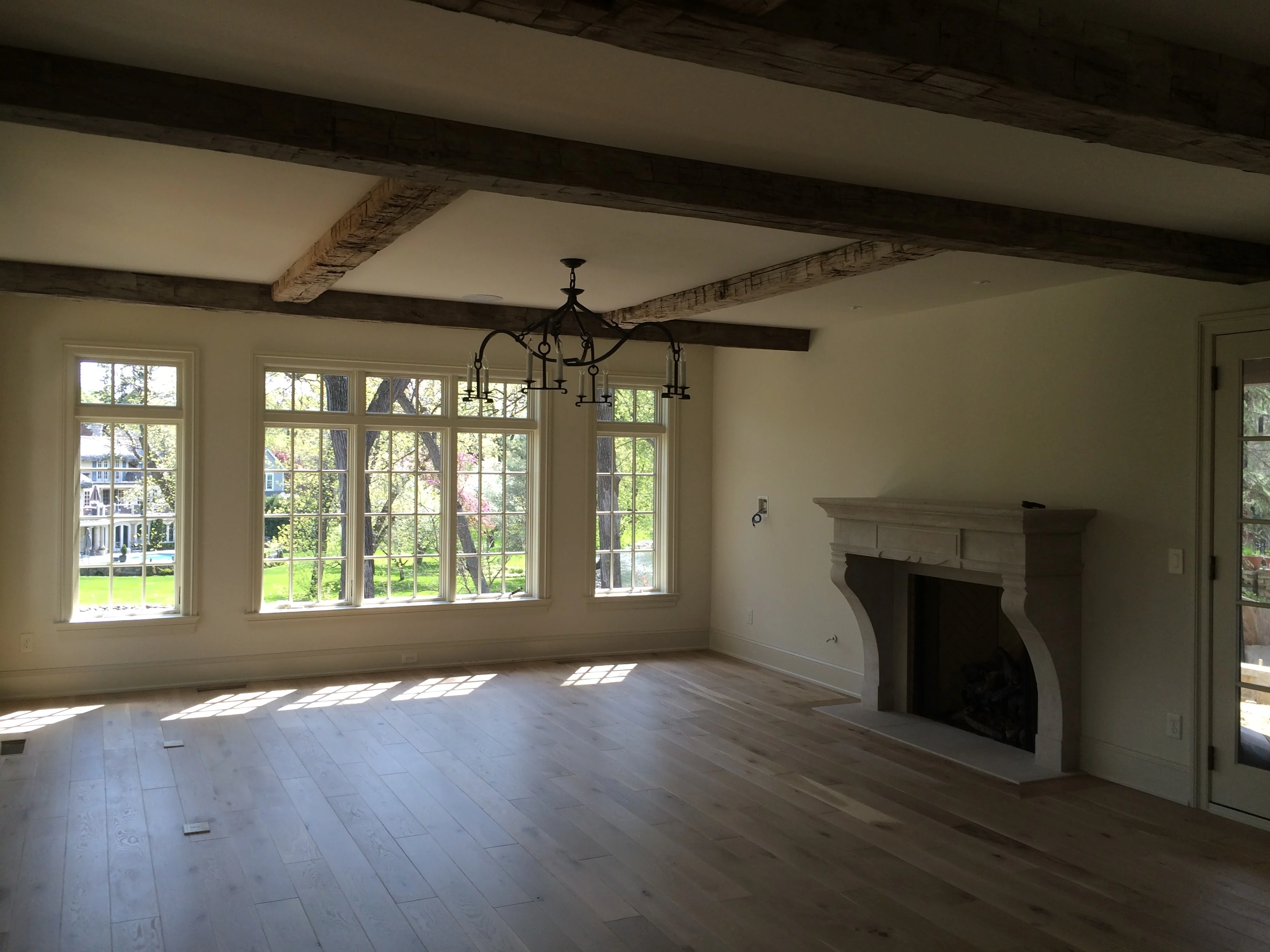 Large multi-pane windows with natural light flooding into a spacious living room with exposed beam ceiling and fireplace.