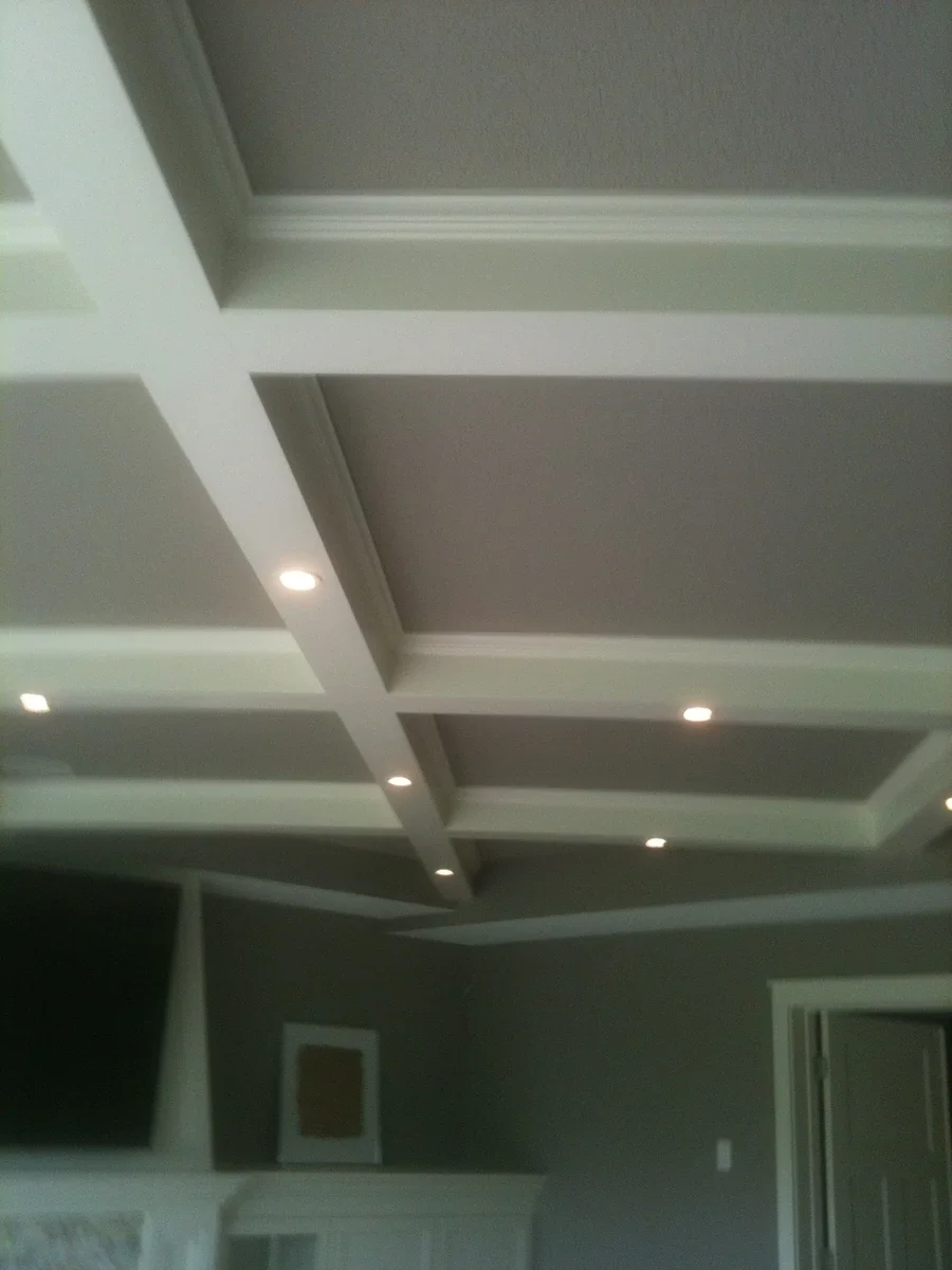 Recessed lighting integrated into a modern coffered ceiling with white beams and gray panels in a residential interior space.